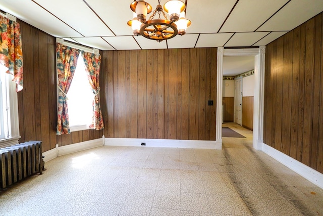 unfurnished room featuring wood walls, radiator heating unit, and an inviting chandelier