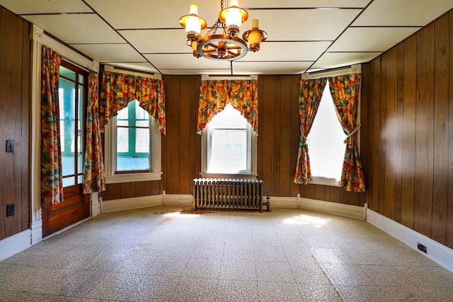 spare room featuring wood walls, radiator heating unit, and a chandelier