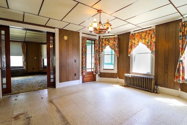 spare room with a chandelier, radiator heating unit, and wood walls