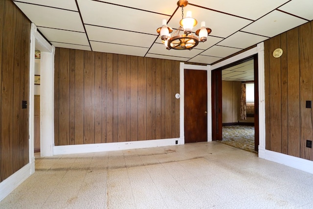 empty room featuring a notable chandelier, wood walls, and a drop ceiling