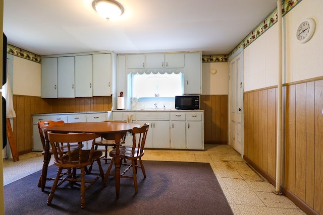 kitchen with white cabinetry, wooden walls, and sink