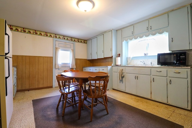 kitchen with white fridge, white cabinetry, wooden walls, and sink