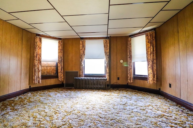 unfurnished room featuring radiator heating unit, carpet floors, a drop ceiling, and wooden walls