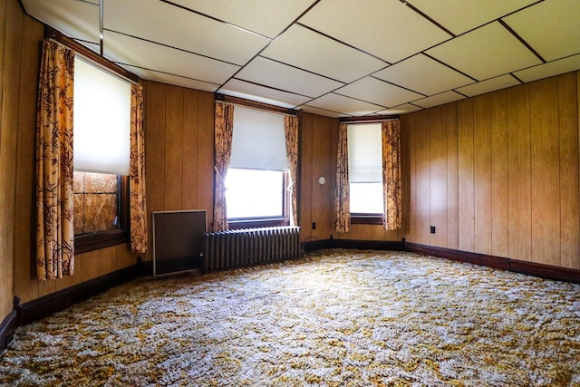 empty room with wood walls, radiator heating unit, and carpet floors