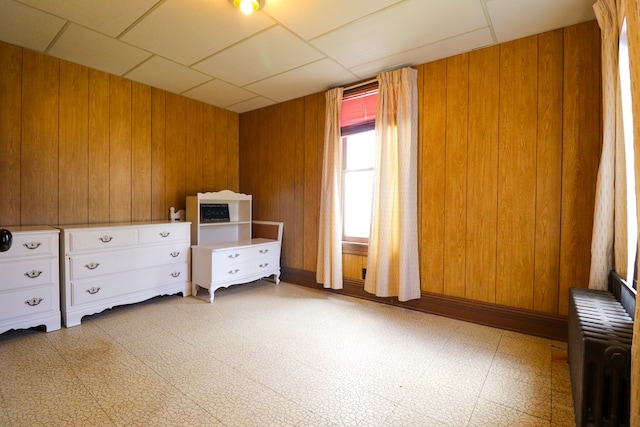 unfurnished bedroom with radiator heating unit, a drop ceiling, and wooden walls