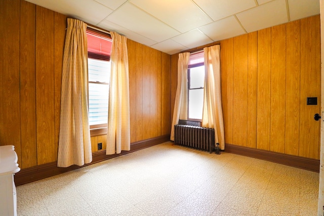 spare room featuring radiator, wood walls, and a drop ceiling