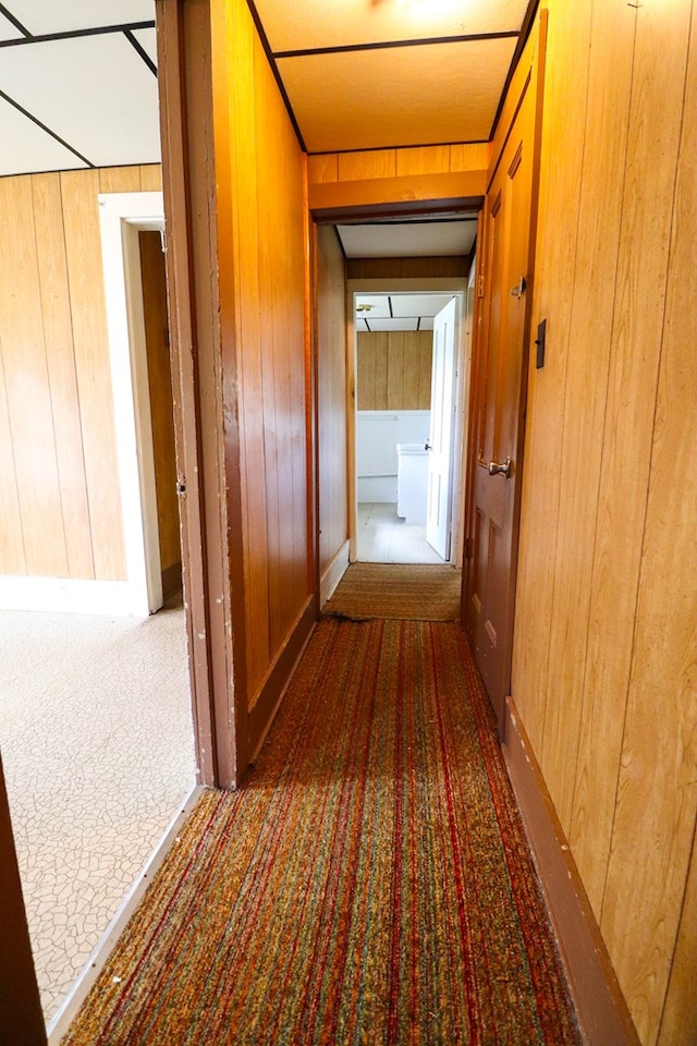 hall featuring dark colored carpet and wooden walls