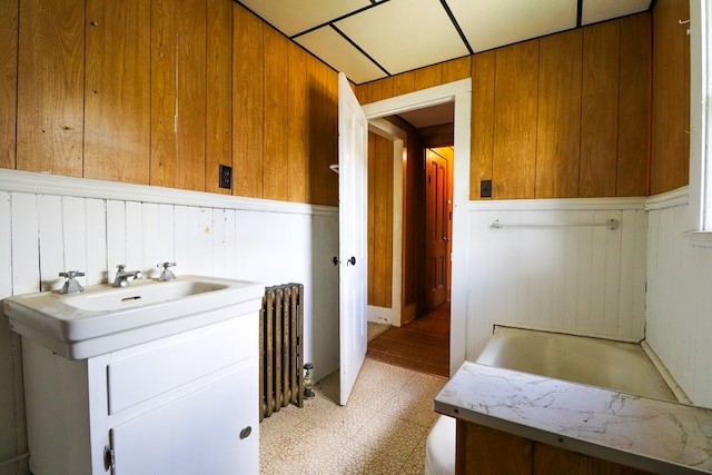 bathroom with wood walls, radiator heating unit, a bathtub, and sink