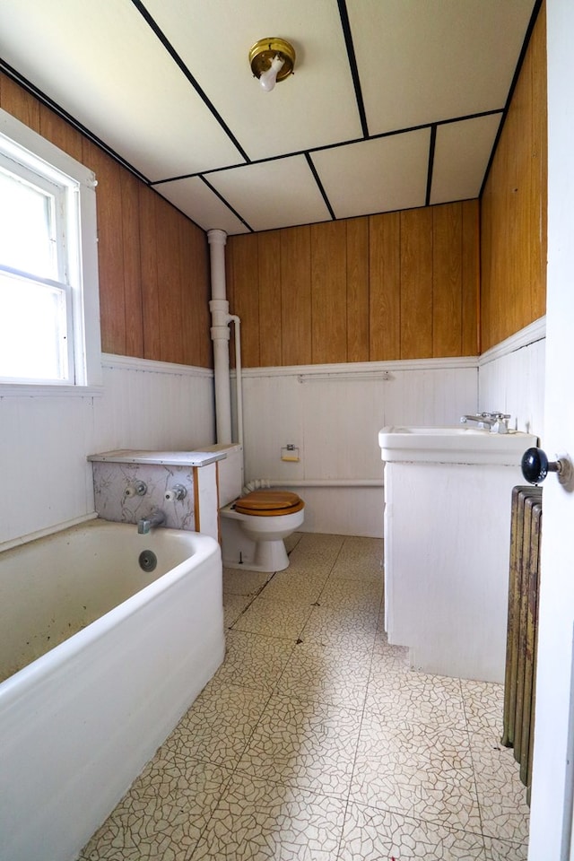 bathroom with a washtub, toilet, sink, and wooden walls