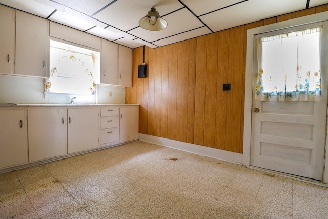 kitchen with a drop ceiling, white cabinetry, sink, and wooden walls