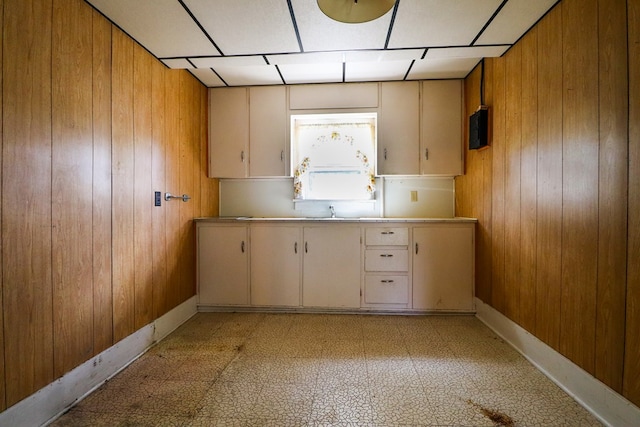 kitchen featuring white cabinetry, cream cabinets, wooden walls, and sink