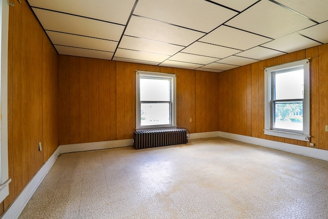 unfurnished room featuring radiator, a wealth of natural light, and wood walls