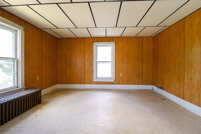 spare room featuring radiator, wooden walls, and a healthy amount of sunlight