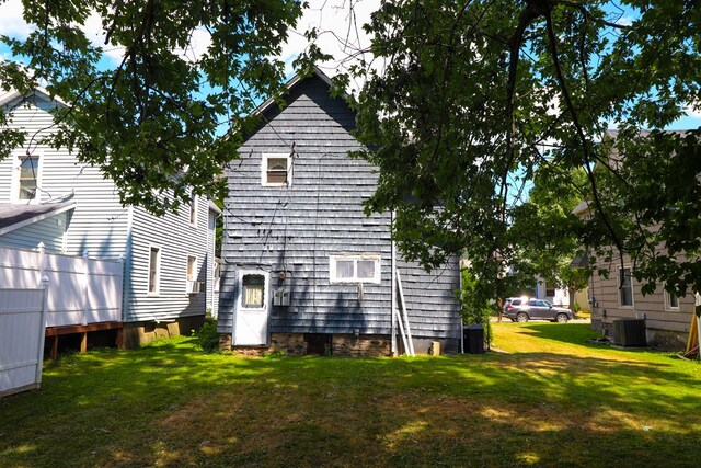 rear view of house featuring central AC unit and a lawn