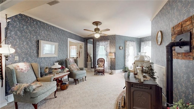 living area with a wood stove, crown molding, ceiling fan, and carpet floors