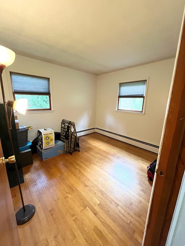 spare room featuring a baseboard heating unit, a wealth of natural light, and light hardwood / wood-style flooring