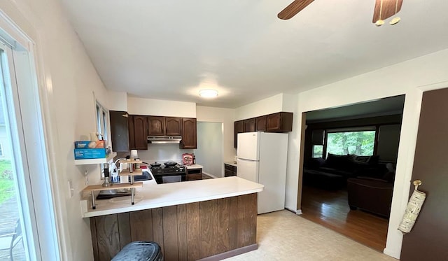 kitchen with dark brown cabinetry, sink, black range oven, kitchen peninsula, and white fridge