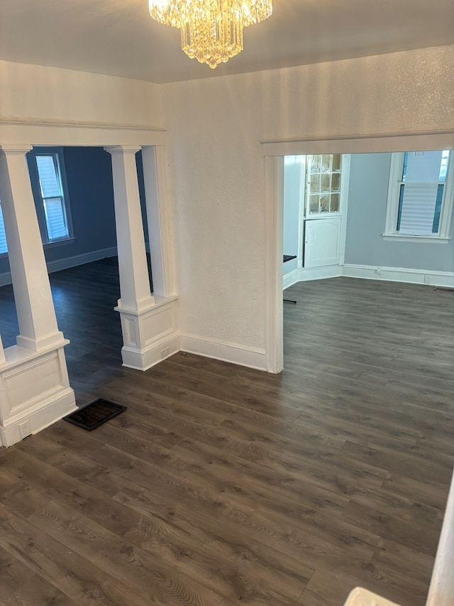 unfurnished living room featuring a notable chandelier, dark hardwood / wood-style floors, and a healthy amount of sunlight