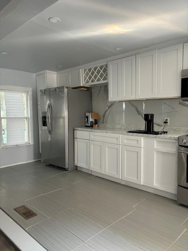 kitchen with appliances with stainless steel finishes, light stone counters, white cabinetry, and tasteful backsplash