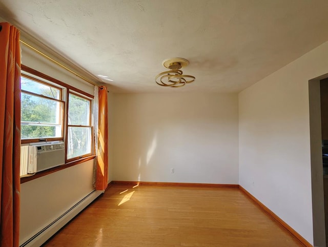 empty room with cooling unit, a baseboard heating unit, and light hardwood / wood-style flooring