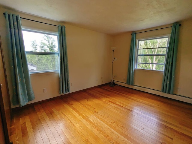 empty room featuring plenty of natural light, a baseboard heating unit, and hardwood / wood-style floors