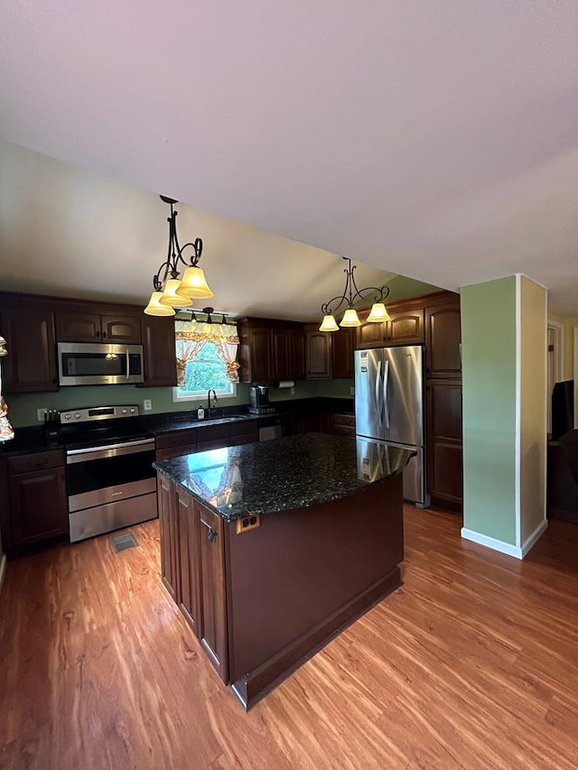 kitchen with hanging light fixtures, a center island, dark brown cabinetry, stainless steel appliances, and light hardwood / wood-style flooring