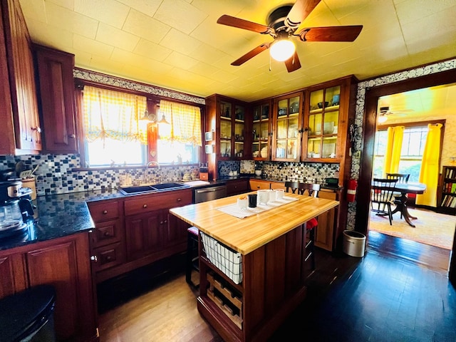 kitchen with wooden counters, wood-type flooring, stainless steel dishwasher, a center island, and sink