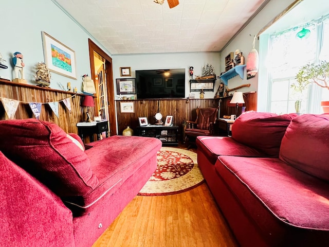 living room with hardwood / wood-style flooring, crown molding, wood walls, and ceiling fan