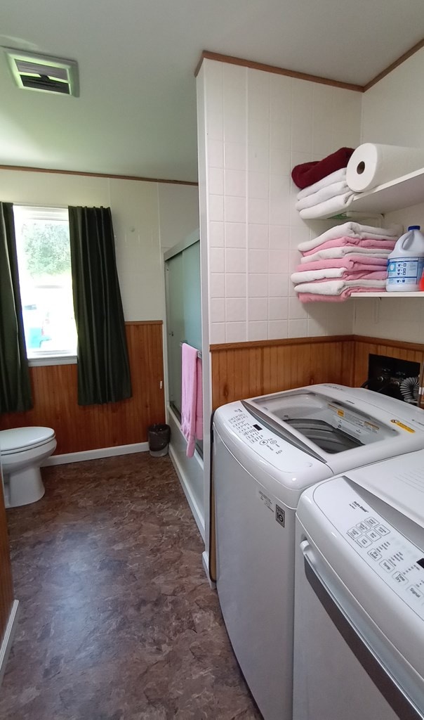 washroom featuring wooden walls, ornamental molding, and washing machine and dryer