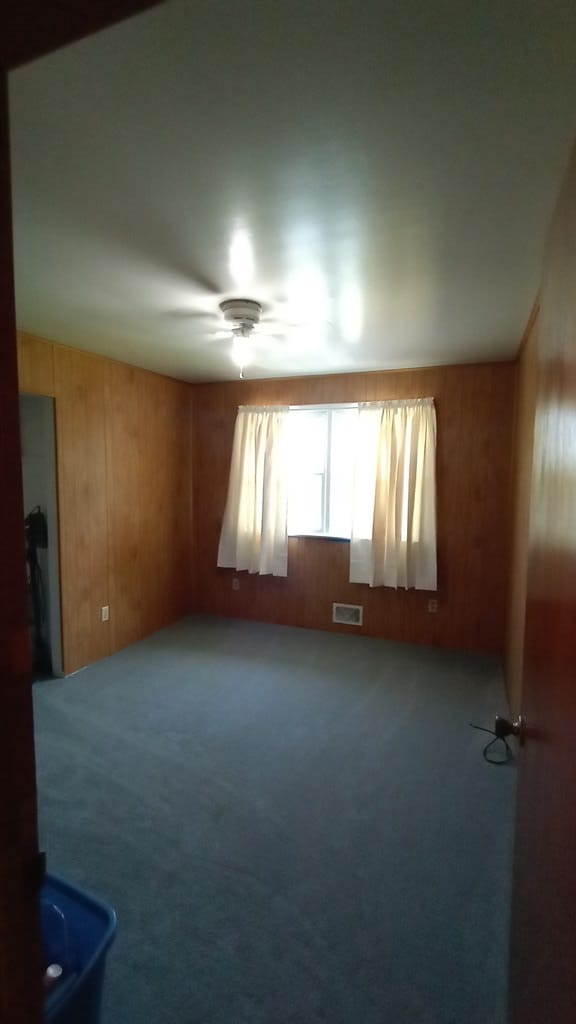 empty room with ceiling fan, wooden walls, and carpet