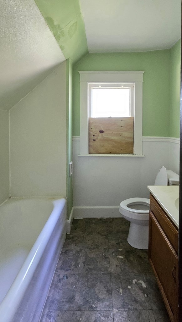 bathroom with toilet, vanity, vaulted ceiling, and a tub