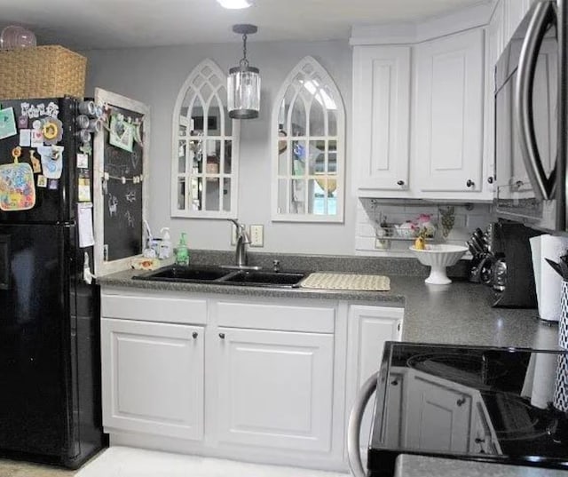 kitchen with black refrigerator, electric stove, sink, and white cabinets