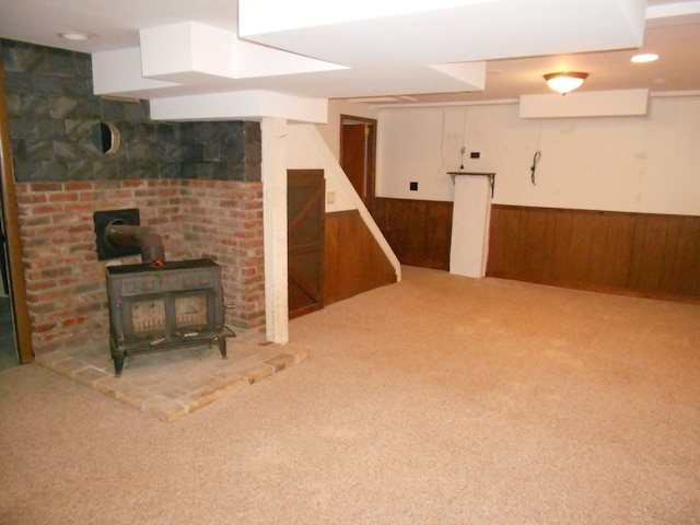 basement featuring light carpet, wood walls, and a wood stove