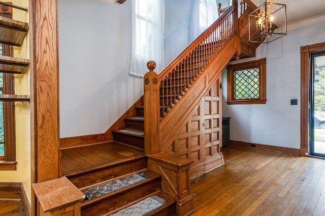 staircase with ornamental molding, hardwood / wood-style floors, and a notable chandelier