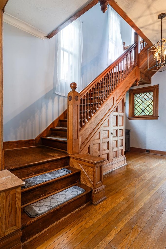 stairs with ornamental molding, wood-type flooring, a chandelier, and a textured ceiling