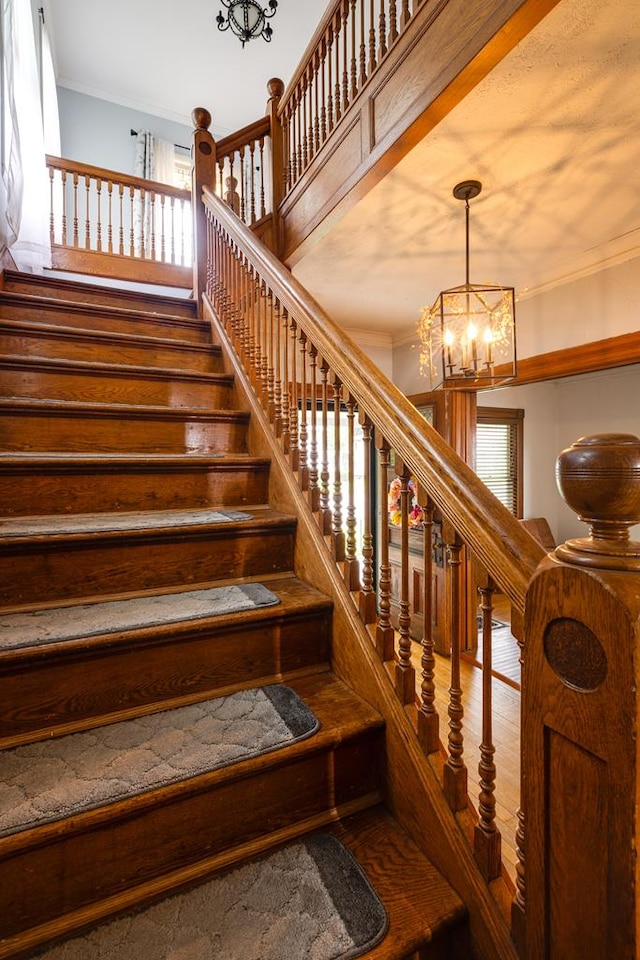 staircase featuring hardwood / wood-style floors, ornamental molding, and a chandelier