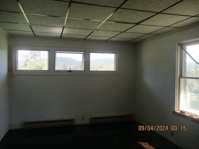 unfurnished room featuring a paneled ceiling, a wealth of natural light, and a baseboard heating unit