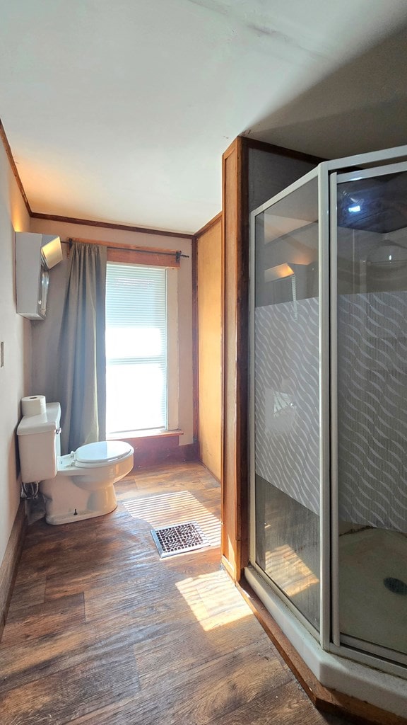 bathroom featuring hardwood / wood-style floors, toilet, and a shower with shower door