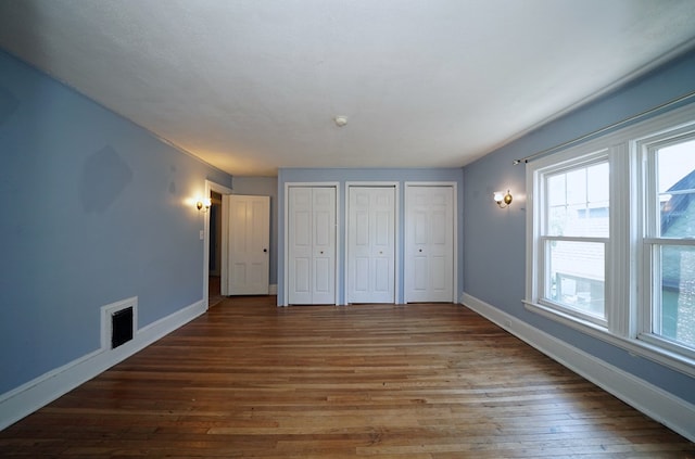 unfurnished bedroom featuring dark wood-type flooring and two closets