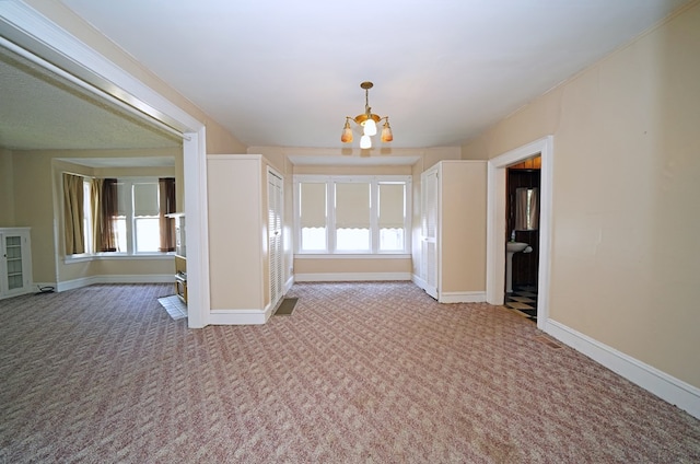 spare room with light colored carpet, a healthy amount of sunlight, and an inviting chandelier