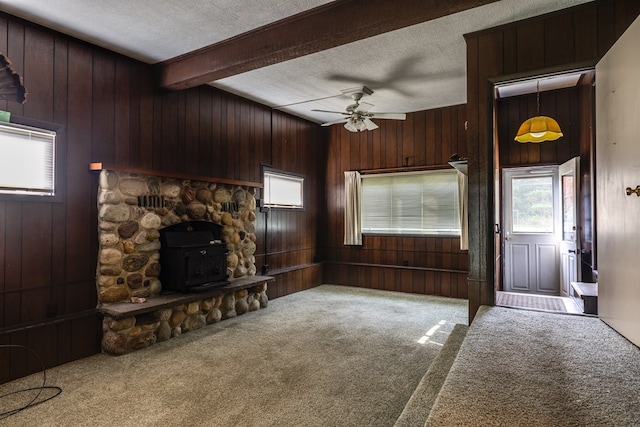 unfurnished living room featuring carpet flooring, beam ceiling, a textured ceiling, and a wood stove