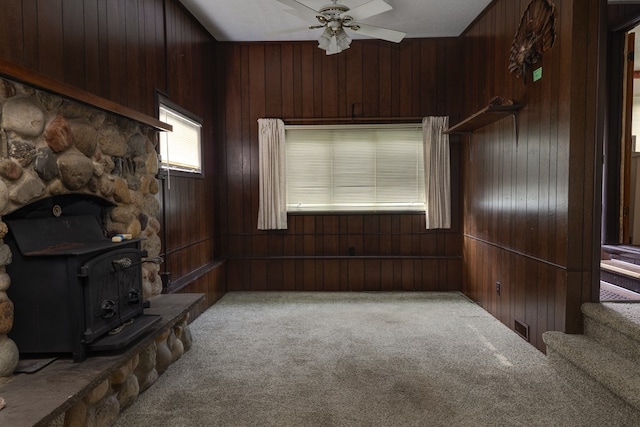 living room with ceiling fan, light colored carpet, wooden walls, and a wood stove