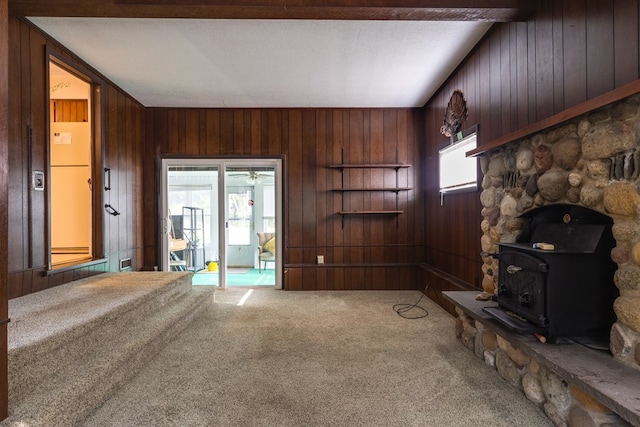 unfurnished living room featuring wood walls, a wealth of natural light, carpet, and a wood stove