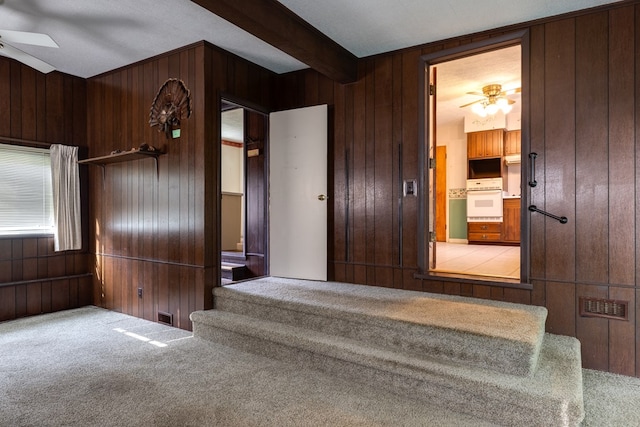 stairway featuring carpet flooring, beamed ceiling, ceiling fan, and wood walls