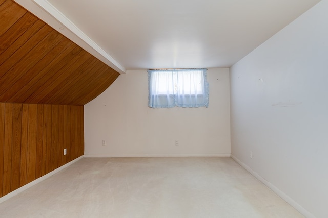 additional living space with light carpet, vaulted ceiling, and wood walls