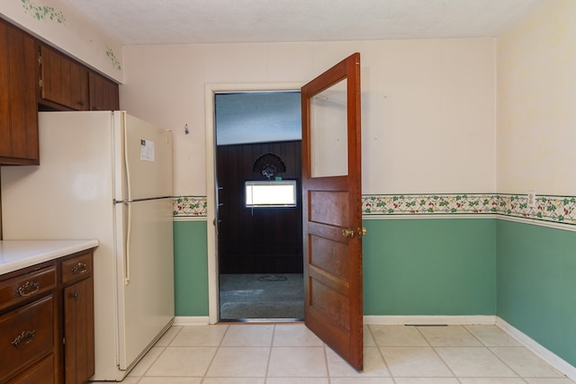 kitchen with white refrigerator, dark brown cabinets, light tile patterned floors, and a textured ceiling