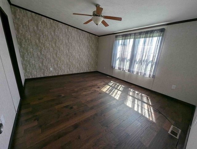 empty room with ceiling fan, dark wood-type flooring, a textured ceiling, and ornamental molding