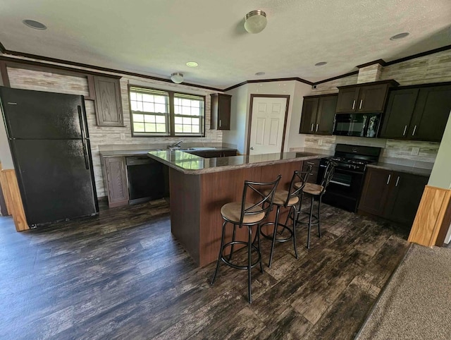 kitchen with a kitchen bar, dark brown cabinetry, dark wood-type flooring, black appliances, and a center island