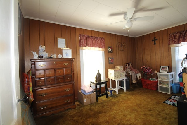 miscellaneous room with dark colored carpet, wooden walls, ceiling fan, and a healthy amount of sunlight