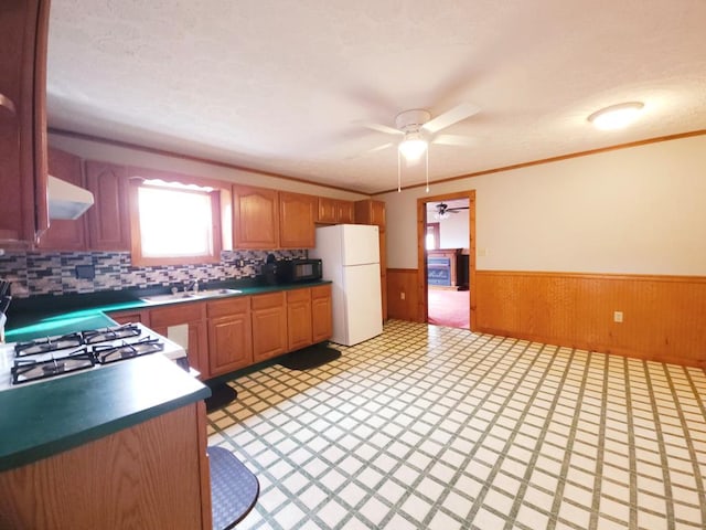 kitchen with wood walls, white appliances, backsplash, sink, and ceiling fan